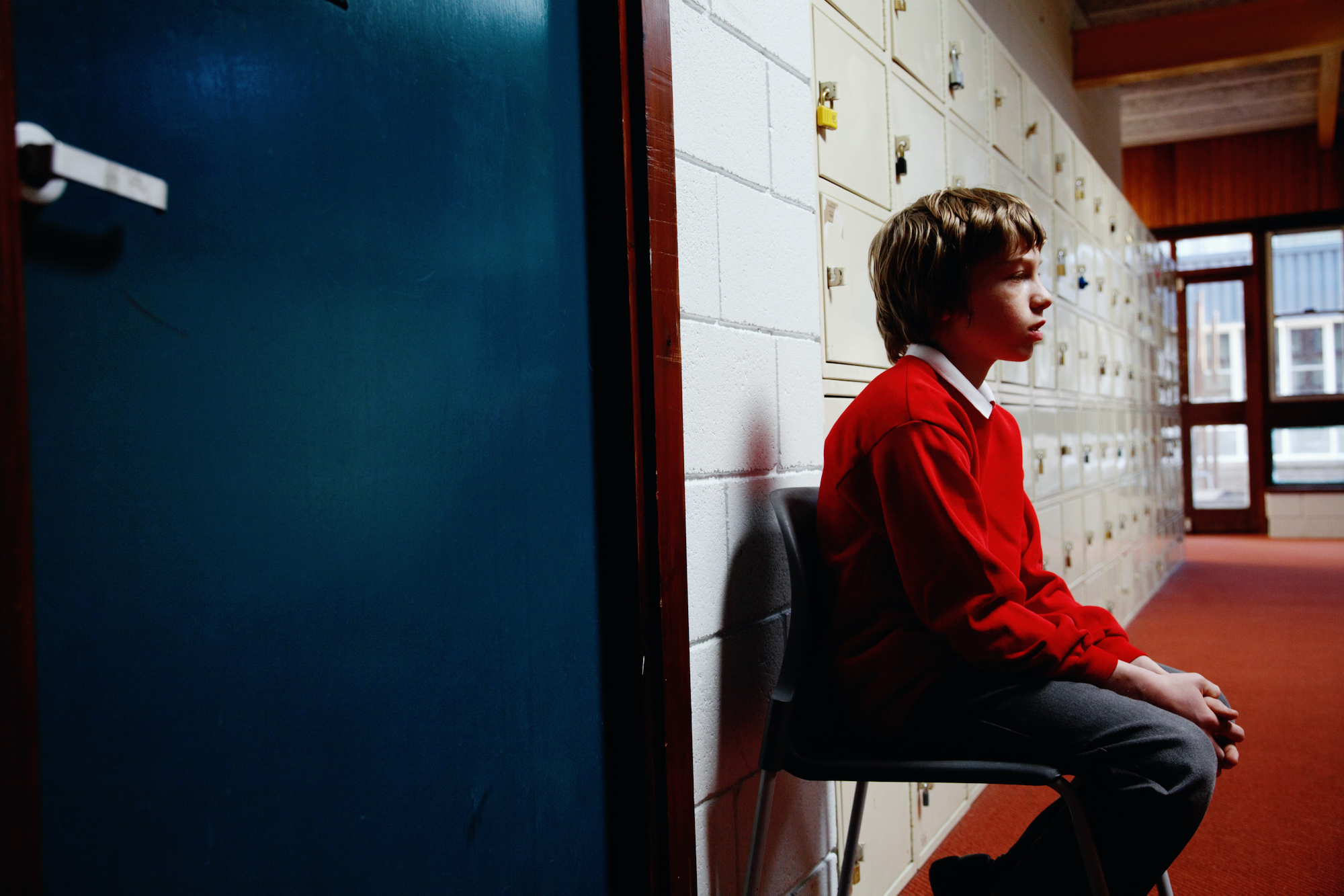 schoolboy sitting on chair in corridor