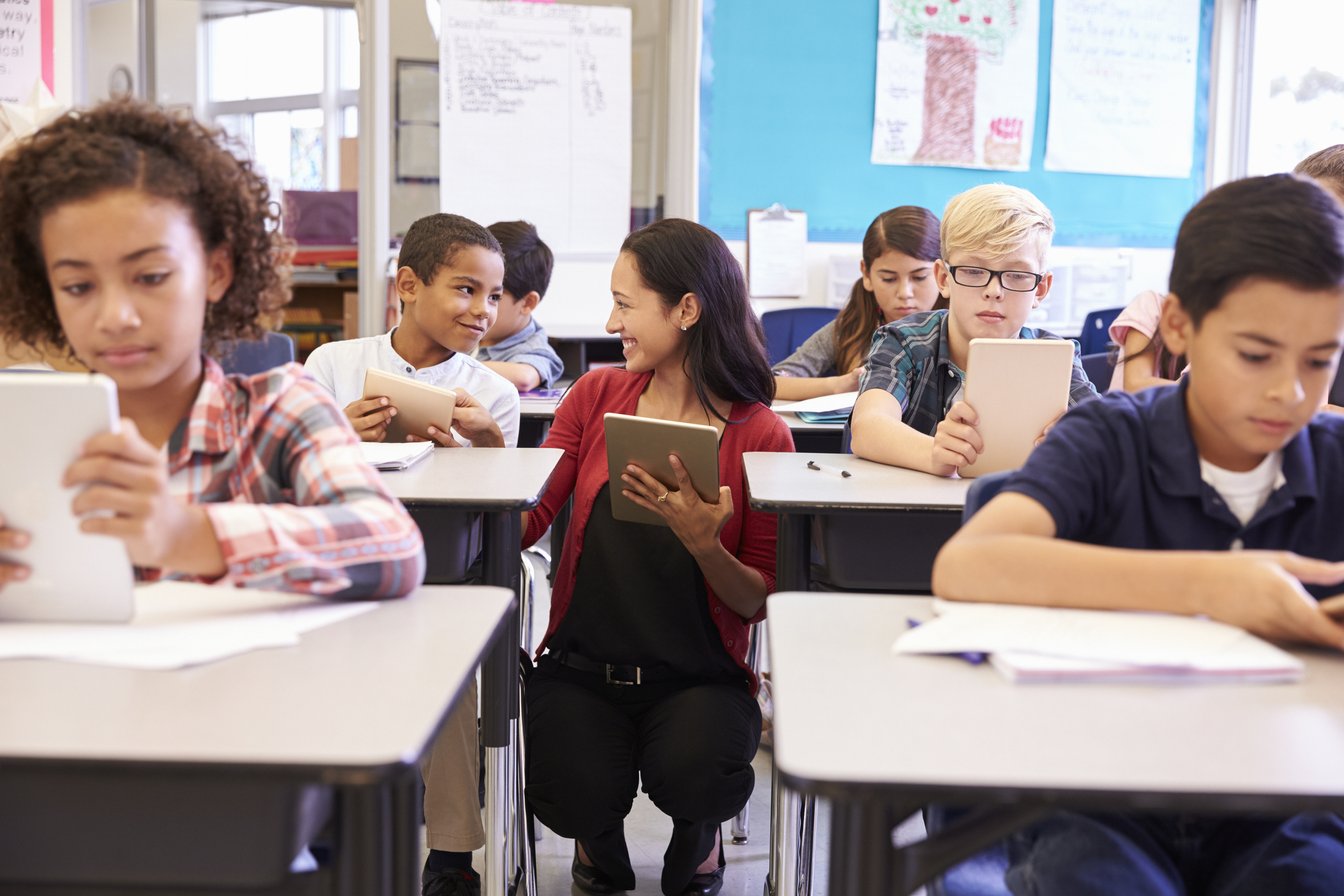 teacher helping students on tablets