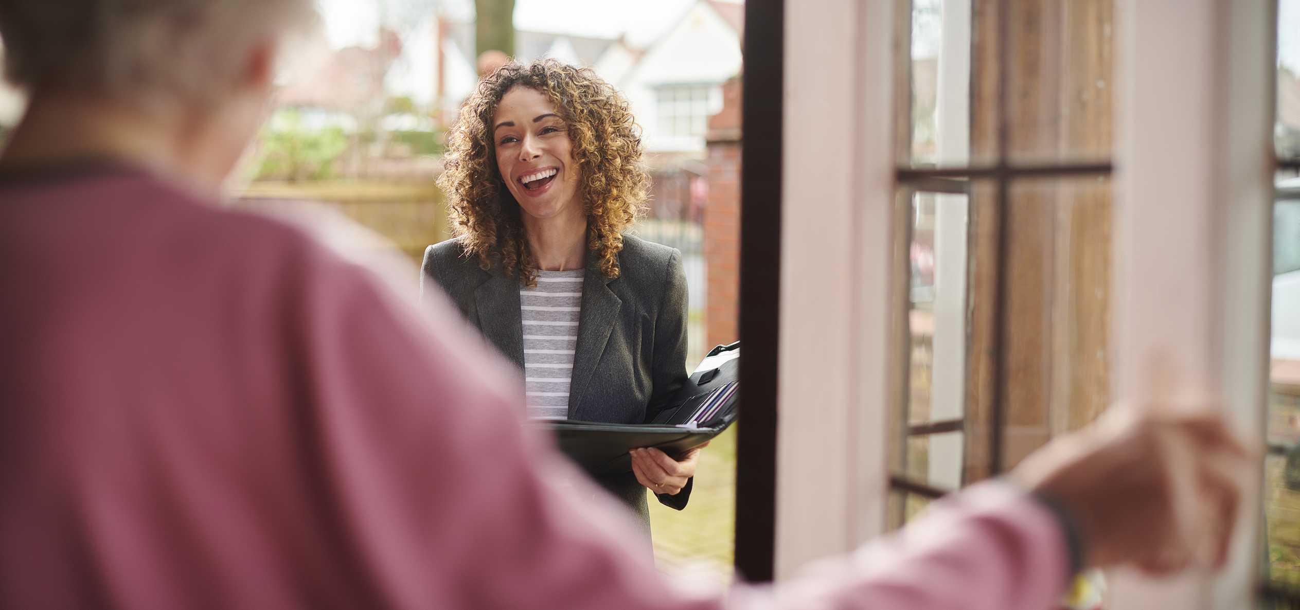 woman holding folder and smailing at door of older woman