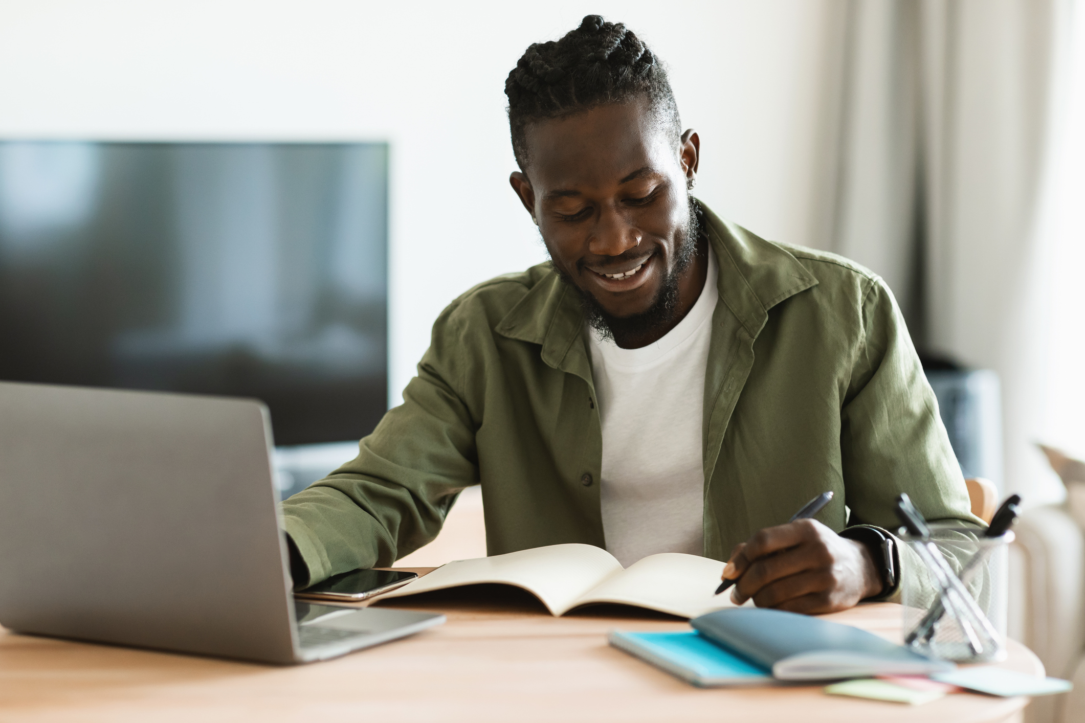 man looking at laptop and writing in notebook