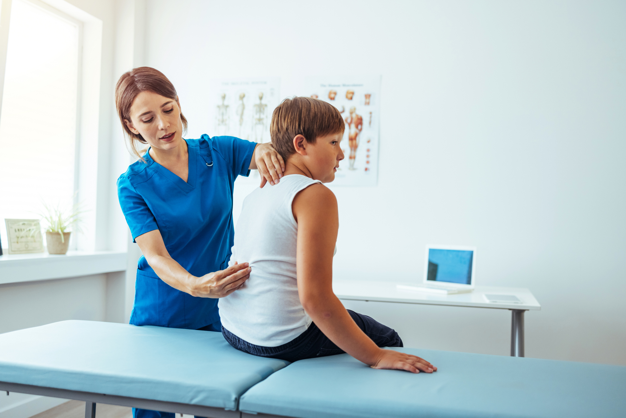 Nurse helping girl with back sitting on table